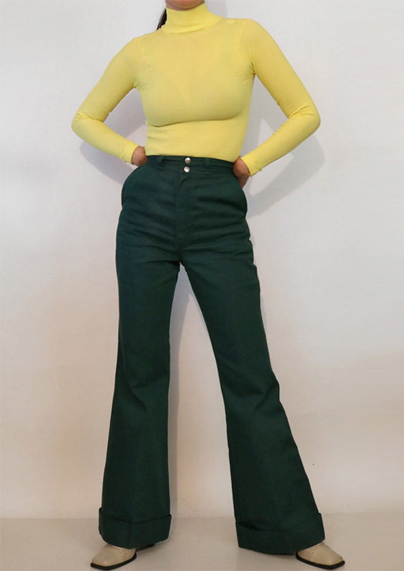 Puede incluir: Una mujer lleva un jersey de cuello alto amarillo brillante y pantalones anchos de color verde oscuro con dobladillo.