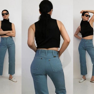 May include: A woman is wearing a black turtleneck top and blue high-waisted jeans. The jeans have a frayed hem.