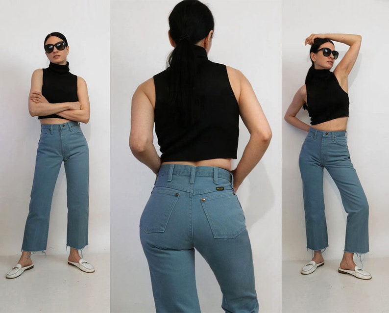 May include: A woman is wearing a black turtleneck top and blue high-waisted jeans. The jeans have a frayed hem.