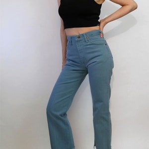 May include: A woman is wearing a black sleeveless turtleneck top and blue denim jeans with a raw hem. She is wearing white leather loafers.