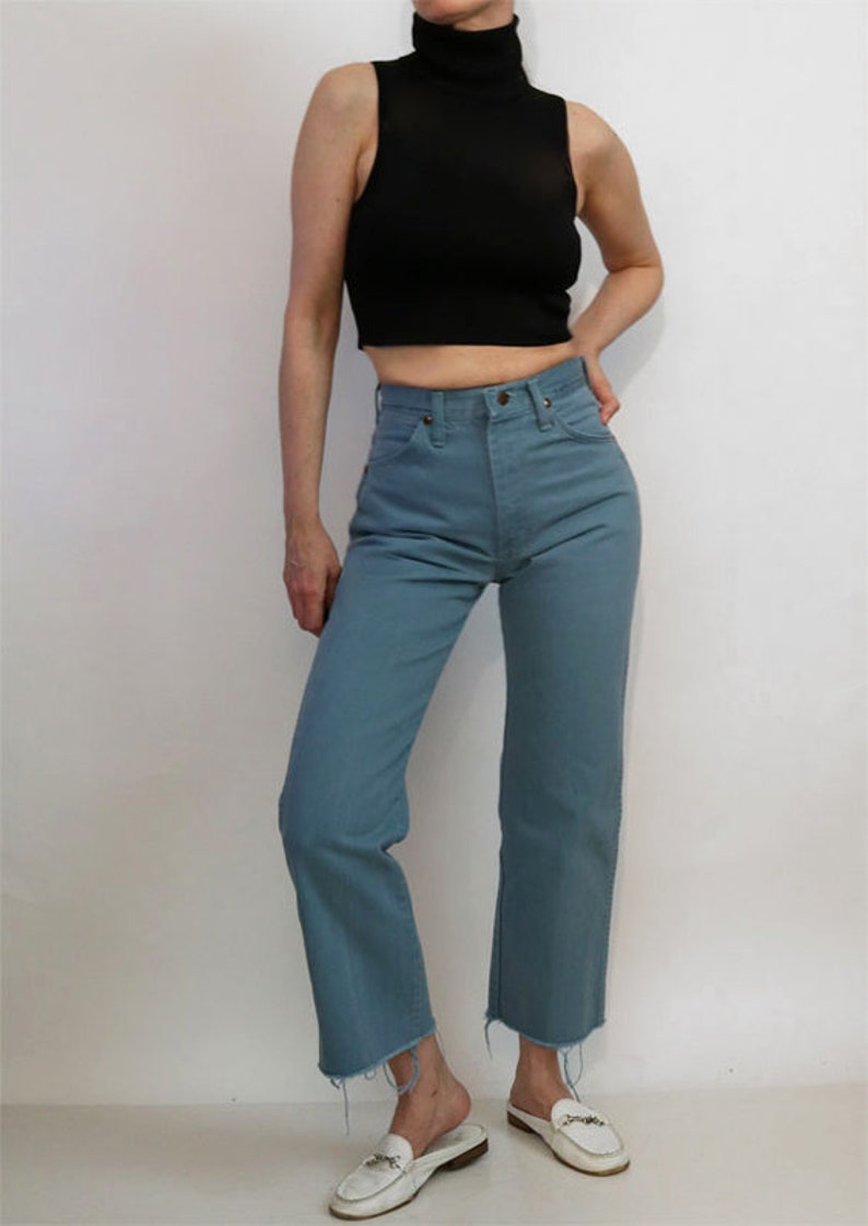 May include: A person wearing a black mock neck shirt and blue jeans with a raw hem.