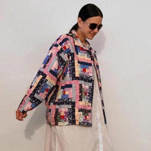 Può includere: Una donna indossa una giacca di patchwork colorata con un motivo geometrico. La giacca ha un colletto e maniche lunghe. La donna indossa un vestito bianco sotto la giacca.