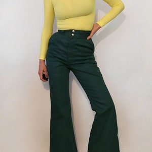 Puede incluir: Una mujer lleva un jersey de cuello alto amarillo brillante y pantalones anchos de color verde oscuro con cintura alta.