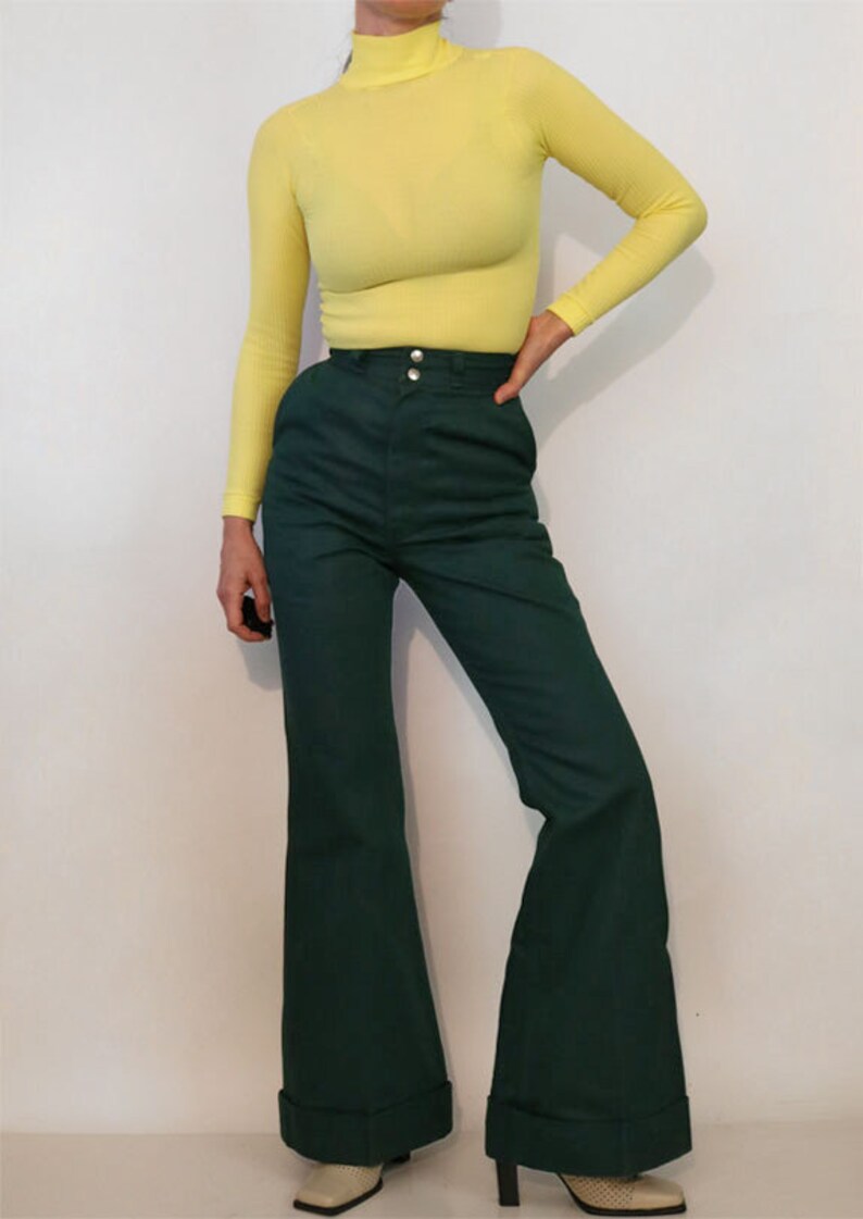 Puede incluir: Una mujer lleva un jersey de cuello alto amarillo brillante y pantalones anchos de color verde oscuro con cintura alta.