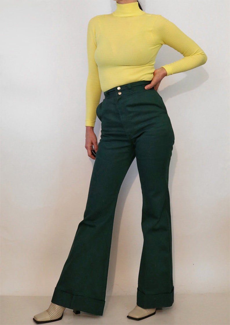 Puede incluir: Una mujer lleva un jersey de cuello alto amarillo brillante y pantalones anchos de color verde oscuro con cintura alta y cierre de bot&oacute;n.