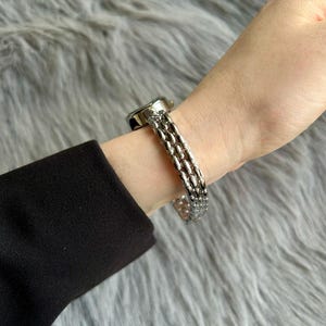 May include: A silver watch with a multi-link band. The watch face is round and has a silver finish.