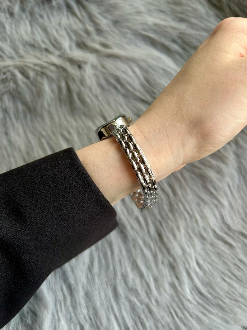 May include: A silver watch with a multi-link band. The watch face is round and has a silver finish.