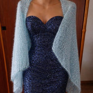 May include: A light blue, open-weave shawl draped over a navy blue sequined dress. The dress has a sweetheart neckline. The shawl appears soft and airy, adding a delicate touch to the formal attire. The dress is knee-length.