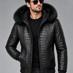 Könnte beinhalten: Eine schwarze Jacke mit texturiertem Krokodilleder-Muster, durchgehendem Frontreißverschluss und einer Kapuze mit dickem, schwarzem Kunstfellbesatz. Das Kleidungsstück verfügt über gerippte Bündchen an Ärmeln und Saum und wird über einem schwarzen Shirt getragen.