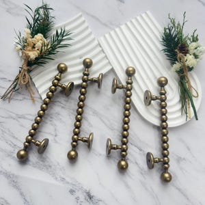 May include: Four antique brass door handles with a beaded design. Each handle has a round base and a series of small spheres leading to a larger sphere at the top. The handles are arranged on a white marble surface.