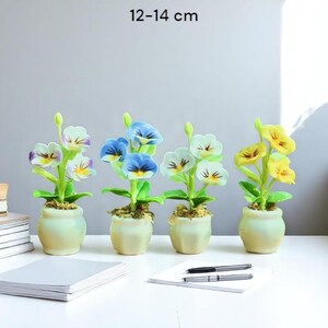 Può includere: Quattro piccole piante artificiali di viole del pensiero in vasi color crema. Le viole hanno petali bianchi, blu e gialli. I vasi sono alti 12-14 cm. Il testo "12-14 cm" è nella parte superiore dell'immagine.