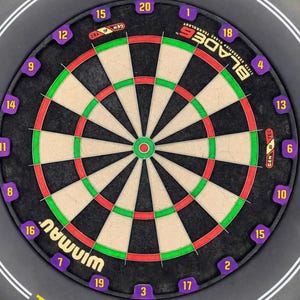 Puede incluir: Un tablero de dardos circular con una superficie negra, con segmentos rojos, verdes y blancos. Los números son morados y la marca "WINMAU" es visible. El tablero está rodeado por un anillo negro con líneas blancas y el logotipo "W".