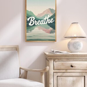 Peut inclure: Une impression encadrée avec une scène de montagne et un lac reflétant les montagnes. Le texte "Breathe" est écrit en blanc sur un fond vert.