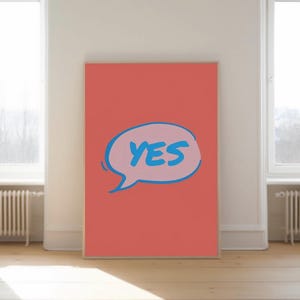 May include: A large, rectangular coral-colored canvas with the word "YES" in a blue speech bubble. The word "YES" is in blue, with a light pink outline. The artwork is displayed in a bright room with natural light.