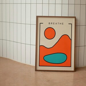 May include: A framed print with a minimalist design featuring a red sun, orange hills, and a teal lake. The print has the word "BREATHE" in black text at the top.