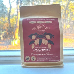 以下が含まれることがあります： Cacao Adventuresの儀式用カカオペーストのパッケージ。 パッケージはタン色で、テキストとカカオポッドのイラストが描かれたマルーン色のラベルが付いています。 テキストには「Sugar Free」、「Vegan」、「Keto Friendly」が含まれています。 正味重量は454gです。