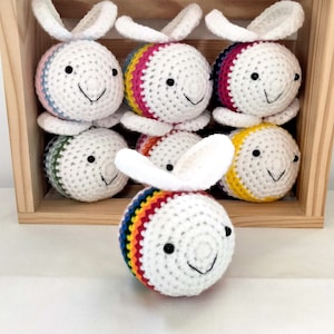 May include: A set of seven crocheted bee toys in a wooden box. The bees are white with rainbow stripes and black eyes.