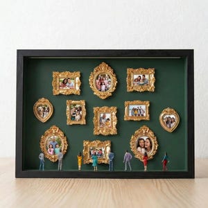 Może przedstawiać: Czarna skrzynka z ciemnozielonym tłem prezentuje kilka zdjęć w złotych ramkach o różnych kształtach. Miniaturowe figurki stoją na dole. Ramki zawierają zdjęcia rodzinne, tworząc spersonalizowaną i dekoracyjną ekspozycję.
