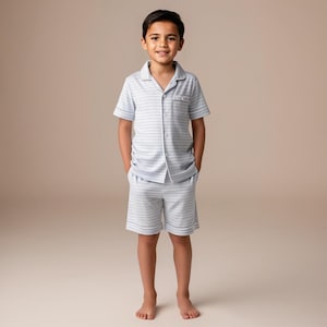 May include: A light blue and white striped pajama set. The set includes a short-sleeved button-down shirt with a chest pocket and matching shorts. The edges of the shirt and shorts are trimmed with white piping.