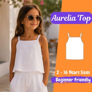 Può includere: Completo bianco Aurelia Top e pantaloncini. Il top ha una scollatura quadrata e spalline sottili. I pantaloncini hanno un girovita con coulisse e tasche. L'immagine include anche un diagramma del top e il testo "2 - 16 Years Sizes Beginner Friendly."