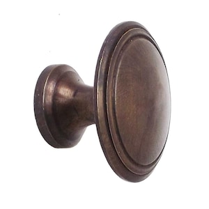 Puede incluir: Un tirador de armario de color bronce con una cara ovalada y una base circular. El tirador tiene un diseño clásico y un acabado metálico cálido. Adecuado para cajones y armarios.