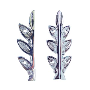May include: Two silver-colored leaf-shaped decorative metal embellishments. Each piece has a central stem with several oval-shaped leaves and small holes. The leaves have a textured surface and a shiny finish, perfect for craft projects.