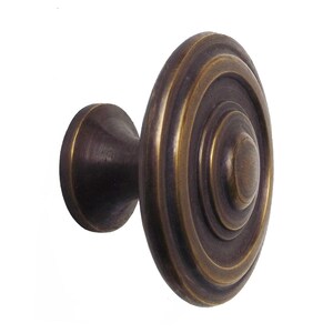 Könnte beinhalten: Ein bronzefarbener Schrankknauf mit kreisförmigem Design. Der Knauf hat konzentrische Ringe auf der Vorderseite und einen abgerundeten Sockel. Die Oberfläche hat ein Vintage-Aussehen, geeignet für Möbelrestaurierung oder Neubauten.