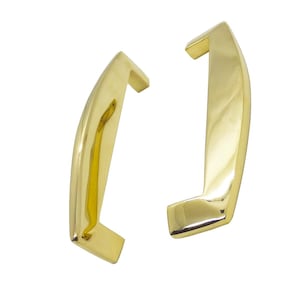 May include: Two polished gold-colored cabinet handles. Each handle has a curved design with a rectangular base and a slightly angled top. The handles are set against a white background.