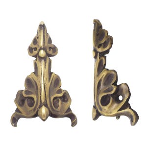 May include: Two antique brass corner brackets with ornate leaf and scroll designs. The brackets are triangular, with a vertical element and a small hole for mounting. The finish is a warm, aged brass colour.