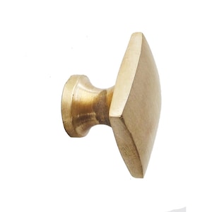 May include: A brass cabinet knob with a diamond-shaped face. The knob has a rounded base and a smooth, polished finish. The hardware is designed for use on drawers, cabinets, or other furniture.