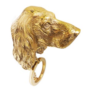 May include: A gold-colored metal dog head key holder with a ring attached to the bottom. The dog's head is detailed with fur and facial features.