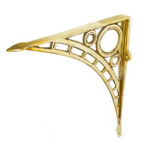 May include: A gold-colored, Art Deco-style shelf bracket. The bracket has a triangular shape with a decorative openwork design featuring circles and rectangular cutouts. The bracket is made of metal and has a small lip at the end.