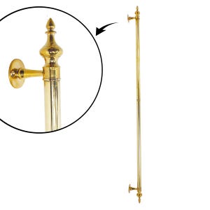May include: A gold-colored, vertical towel bar with decorative finials and wall mounts. The bar is a long, slender pole with ornate detailing at the top and bottom, and at the wall mounts. The finish is shiny and reflective.