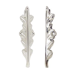 May include: Two silver-coloured, leaf-shaped decorative metal pieces. Each piece has a detailed, veined leaf design with a curved shape and small holes for mounting. The pieces are displayed against a white background.
