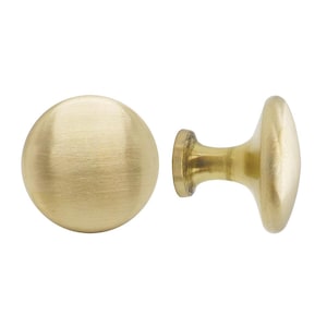 May include: Two brass cabinet knobs. One is a round knob, and the other is a knob with a cylindrical base and an oval head. Both knobs have a brushed finish and a warm, golden color, suitable for furniture or cabinetry.