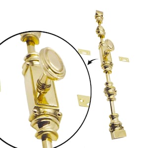 May include: A polished brass window stay with an oval knob and decorative detailing. The stay is shown with two small brass plates, likely for mounting. The hardware has a bright, reflective finish.