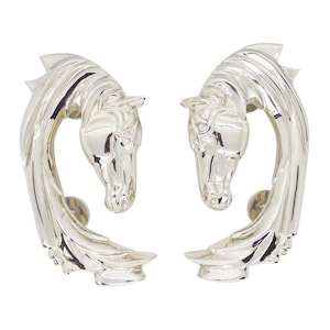 Peut inclure: Deux poignées de porte argentées, chacune en forme de tête de cheval avec une crinière fluide. Les poignées sont incurvées et ont une petite base ronde pour le montage. Le design est détaillé et réfléchissant, suggérant une finition en métal poli.