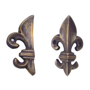 May include: Two antique bronze fleur-de-lis decorative hardware pieces. The hardware has a detailed design with a classic shape. The bronze finish gives the hardware an aged, vintage look. The hardware is likely used for furniture or decorative purposes.