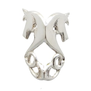 Op de afbeelding: Een zilverkleurige metalen decoratieve sluiting met twee paardenkoppen die naar elkaar toe kijken. De paarden zijn bij de nek verbonden en hebben een decoratief wervelontwerp aan de onderkant. De sluiting heeft twee bevestigingsgaten.