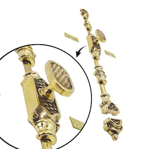 Op de afbeelding: Messing raamgrendel met een decoratief ontwerp. De grendel heeft een gedetailleerd, gestructureerd patroon op de handgreep en een rechthoekig lichaam. Inclusief twee kleine, rechthoekige montageplaten.