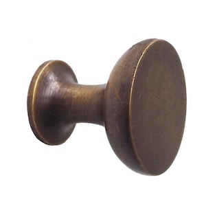 Może przedstawiać: Mosiężny uchwyt do szafki o owalnym kształcie i krótkiej, cylindrycznej szyjce. Podstawa uchwytu jest okrągła. Wykończenie ma lekko postarzany wygląd. Prosty, funkcjonalny design.