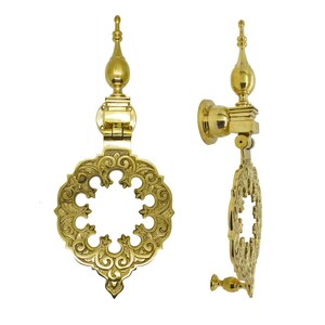 May include: Two ornate brass door knockers. The knockers feature an openwork design with intricate floral patterns. Each knocker has a decorative finial and a hinged mechanism for striking the door. The brass has a polished, golden finish.