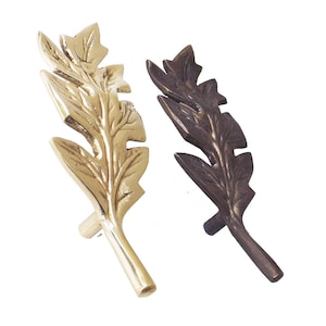May include: Two ornate brass leaf-shaped cabinet pulls, one in a polished gold finish and the other in a dark antique brass finish.