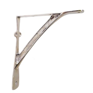 May include: A silver-colored metal shelf bracket with a curved support arm. The bracket has a decorative design and is suitable for supporting shelves. The bracket is approximately 8 inches long and 6 inches high.