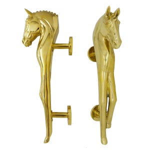 May include: Two golden door handles, each shaped like a horse. The handles are detailed with a horse's head and body, and are mounted on round plates with a horizontal bar for gripping. The handles are made of a shiny, reflective metal.