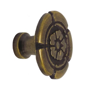 Op de afbeelding: Bronzen kastknop met een bloemmotief. De knop heeft een afgeronde voorkant met een gedetailleerd bloempatroon en een cilindrische steel. De afwerking heeft een licht verouderd uiterlijk, met een diameter van ongeveer 3,8 cm.