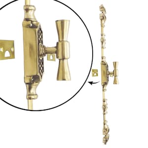 Op de afbeelding: Een messing raamgrendel met een decoratief ontwerp. Het slot heeft een handvat en een bijpassende sluitplaat. De hardware heeft een warme goudkleur en is ontworpen voor een raam. De afbeelding bevat een close-up van het slot.