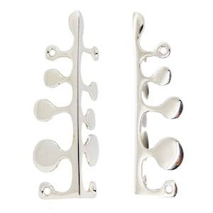 May include: Two silver-colored, abstract metal decorative pieces. Each piece has a vertical stem with rounded, organic shapes branching off. The pieces have small holes at the top and bottom, suggesting they are designed to be attached to something.