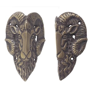 May include: Two antique brass ram head cabinet pulls. Each pull features a detailed ram head with curved horns and a textured surface. The pulls are designed to be mounted on a cabinet or drawer, adding a rustic or vintage touch.