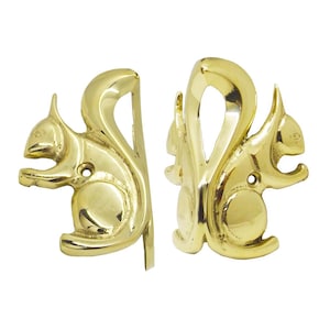 May include: Two shiny, gold-colored squirrel-shaped bookends. The bookends are made of metal and have a smooth, reflective surface. Each squirrel is depicted in a sitting position with its tail curved upwards. The bookends are designed to hold books upright.